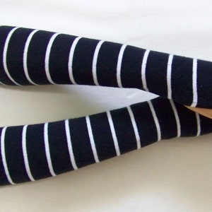 Puede incluir: Un par de calentadores de brazos a rayas blancas y negras. Los calentadores de brazos están hechos de un tejido suave y de punto y son perfectos para mantener los brazos calientes en los meses más fríos.