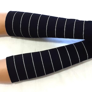 Puede incluir: Un par de guantes sin dedos negros con rayas blancas. Los guantes están hechos de un tejido suave y elástico y son perfectos para añadir un toque de estilo a cualquier atuendo.