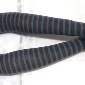May include: A pair of striped arm warmers. The arm warmers are dark brown with teal stripes. The arm warmers are displayed on a mannequin, with the fingers visible.
