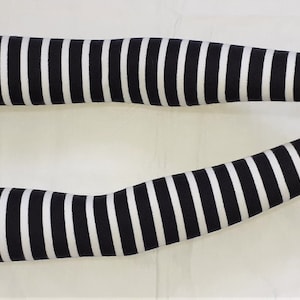 Puede incluir: Un par de calentadores de brazo a rayas blancas y negras. Los calentadores de brazo están hechos de un tejido elástico y son lo suficientemente largos como para cubrir todo el antebrazo.