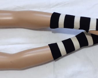 May include: A pair of black and white striped fingerless gloves. The gloves are on a mannequin arm, with the stripes running horizontally. The gloves are made of a soft material and cover the wrist and part of the hand.