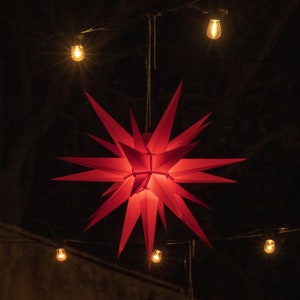 May include: A red paper star hanging from the ceiling with string lights around it.