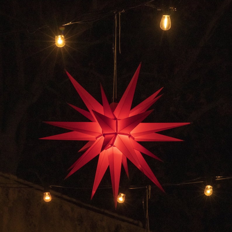 May include: A red paper star hanging from the ceiling with string lights around it.
