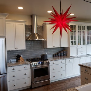 May include: A modern kitchen with white cabinets, stainless steel appliances, and a granite countertop. A red star-shaped light fixture hangs from the ceiling.