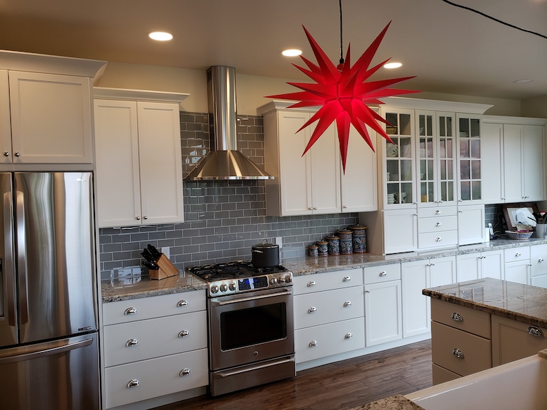 May include: A modern kitchen with white cabinets, stainless steel appliances, and a granite countertop. A red star-shaped light fixture hangs from the ceiling.