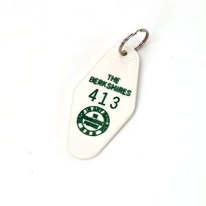 May include: White vintage motel keychain with a silver key ring. The keychain has green text that reads "THE BERKSHIRES" above the number "413" and a circular logo. The keychain is a retro style souvenir.