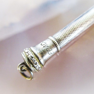 May include: Close-up of a silver mechanical pencil. The pencil has a textured body and a detailed tip with the engraved letters "EDAC". A small loop is attached to the tip. The pencil is set against a soft, blurred background.