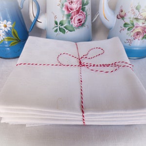 May include: A stack of white linen tea towels tied with red and white twine. The towels are folded neatly and have a subtle embroidered design.