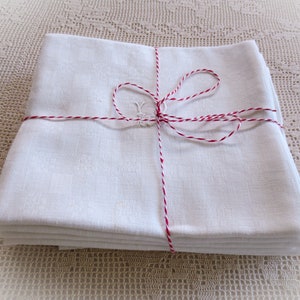 Può includere: Un mucchio di tovaglioli di lino bianco legati insieme con uno spago rosso e bianco. I tovaglioli sono piegati a metà e impilati uno sopra l'altro.