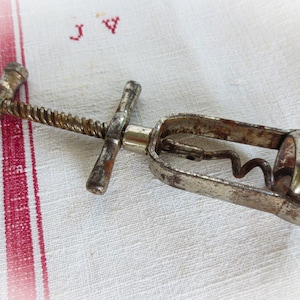 May include: A vintage metal corkscrew with a t-shaped handle and a worm screw. The corkscrew is rusty and shows signs of wear.