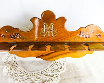 Könnte beinhalten: Wandregal aus Holz mit floralem Design und dem goldenen Buchstaben "M". Das Regal hat mehrere kleine, gebogene Aussparungen. Das Holz hat eine warme, natürliche Oberfläche.