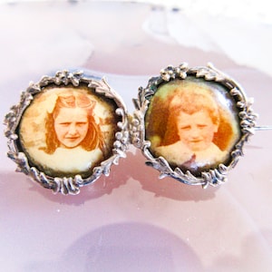 May include: Two silver locket-style pendants with floral designs. Each pendant features a portrait of a child, one girl and one boy, in a cameo-style setting.