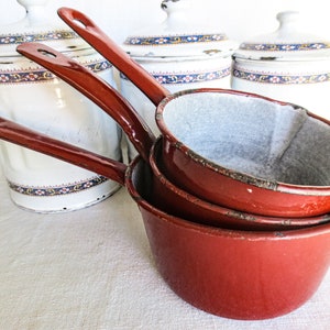 May include: Set of four red enamel saucepans with handles. The saucepans are nested together and have a worn, vintage look.