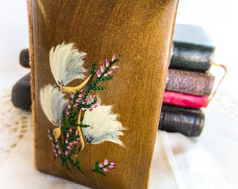 May include: A brown wooden box with a hand-painted floral design. The artwork features white, yellow, and pink flowers with green stems. The box is rectangular and has a curved top. Other boxes are stacked in the background.