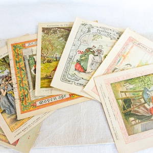 May include: A collection of antique French prints, featuring colorful illustrations and text. The prints depict scenes from history and literature, with titles like "Art du Moyen Age" and "Les Victimes du Devoir". The prints are arranged on a light-colored surface.