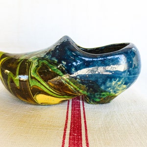 May include: A blue, green, and brown ceramic Dutch shoe planter. The shoe is glazed and has a marbled pattern.