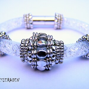 May include: A white beaded bracelet with a silver magnetic clasp and a silver bead cluster in the centre.