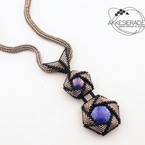 Op de afbeelding: Een zilveren ketting met een zwarte en zilveren hanger met twee zeshoekige vormen met blauwe en paarse stenen.