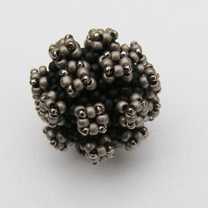 May include: A small, round, beaded ornament made of black and silver beads. The beads are arranged in a cluster of small flowers.