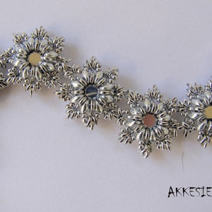 May include: Silver bracelet featuring a series of mirrored snowflake-shaped charms. The bracelet has a silver clasp and a silver bead at the end.