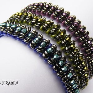 May include: Three beaded bracelets in blue, green, and purple. Each bracelet has a repeating pattern of metallic beads. The bracelets are stacked, showing the intricate design and colour variations. The text "AKKESIERADEN" is in the bottom left corner.