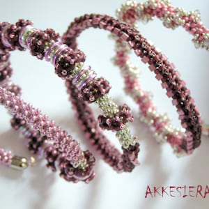 Könnte beinhalten: Drei rosafarbene und violette Perlenarmbänder mit silbernen Akzenten. Die Armbänder sind zusammengerollt und haben einen zarten, femininen Look.