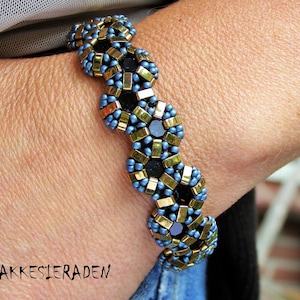 Könnte beinhalten: Ein blaues und goldenes Perlenarmband mit schwarzen Akzenten. Das Armband besteht aus kleinen, runden Perlen, die in einem komplizierten Muster miteinander verwoben sind. Das Armband wird am Handgelenk getragen.