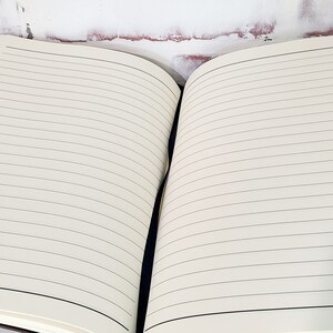 Pu&ograve; includere: Quaderno aperto con pagine a righe color crema. Le pagine hanno sottili linee nere orizzontali. Il quaderno &egrave; aperto, rivelando le pagine interne. La rilegatura &egrave; scura e le pagine sono pulite e pronte per la scrittura.