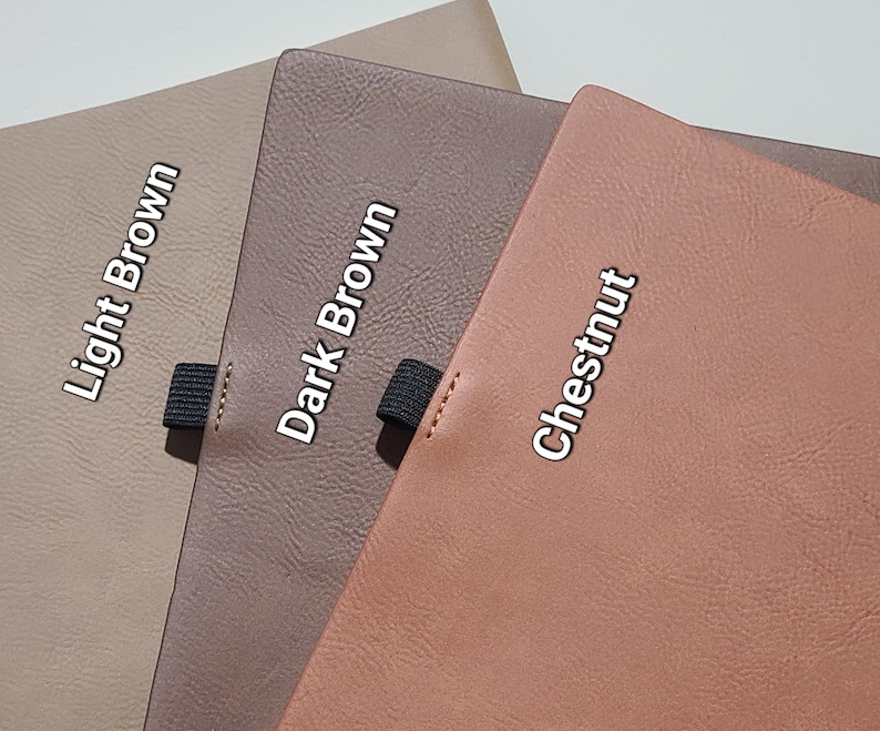 Pu&ograve; includere: Primo piano di tre quaderni in pelle nei colori marrone chiaro, marrone scuro e castagno. Ogni quaderno ha un elastico nero e il nome del colore stampato sulla copertina.