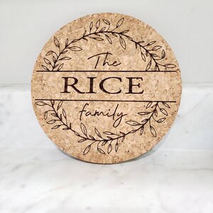 May include: A round cork trivet with a decorative wreath design and the text "The RICE family" engraved in the center.