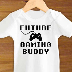 May include: White baby onesie with black text that reads "FUTURE GAMING BUDDY" and a black pixelated video game controller graphic.