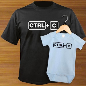 May include: A black t-shirt with the text "CTRL+C" in white, and a light blue baby onesie with the text "CTRL+V" in black.