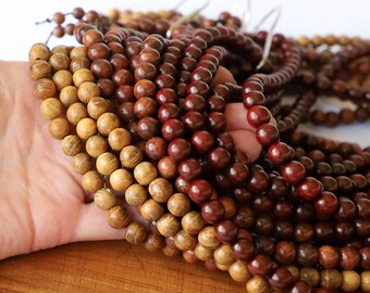 May include: Close-up of multiple strands of wooden beads in varying shades of brown. The beads are round and appear to be strung together. The color ranges from light tan to deep reddish-brown. The beads are held in a hand, with a white background.