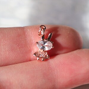 Puede incluir: Un charm de oro rosa con una peque&ntilde;a figura de ni&ntilde;a con un gran cristal transparente en el centro. El charm tiene un bucle en la parte superior para sujetarlo a un collar o pulsera.