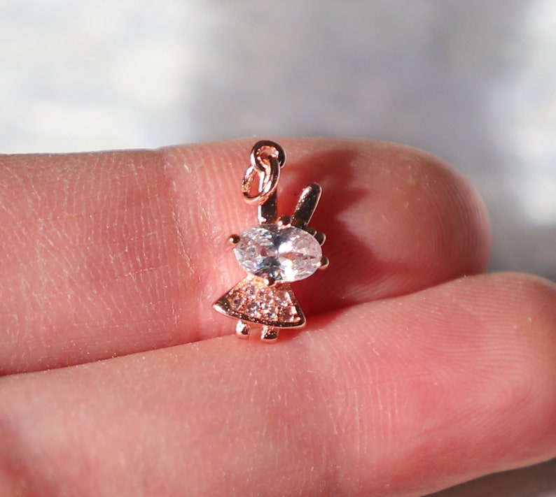 Puede incluir: Un charm de oro rosa con una peque&ntilde;a figura de ni&ntilde;a con un gran cristal transparente en el centro. El charm tiene un bucle en la parte superior para sujetarlo a un collar o pulsera.