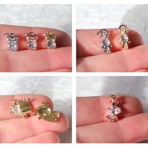 Puede incluir: Surtido de colgantes de amuleto de oro y plata con varios dise&ntilde;os, incluyendo un b&uacute;ho, un &aacute;ngel, una vaca y un conejo. Cada amuleto est&aacute; adornado con brillantes diamantes de imitaci&oacute;n transparentes.