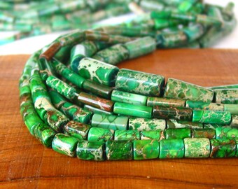 Könnte beinhalten: Eine Strähne grüner und brauner Jaspisperlen, jede Perle hat eine zylindrische Form mit einem marmorierten Muster.