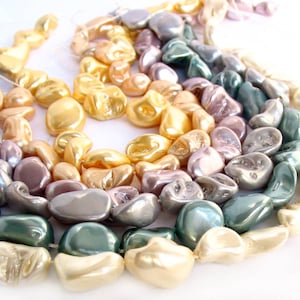 May include: A strand of iridescent, pearlescent beads in shades of gold, lavender, and teal. The beads are irregularly shaped and have a smooth, polished finish.
