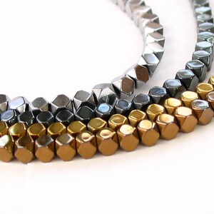 May include: Three strands of faceted gemstone beads in gold, silver, and black. The beads are hexagonal in shape and have a metallic sheen.