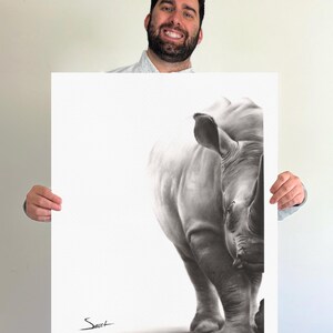 May include: A rectangular art print featuring a detailed black and white charcoal-style drawing of a rhinoceros. The animal is positioned on the right side of the white paper, with a signature in the bottom left corner that reads Sweet.