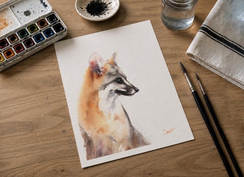 May include: A watercolor painting on white paper depicting a fox in profile, rendered in shades of orange, brown, and grey. The artwork features a soft, blended style with visible brushstrokes and a small orange signature in the bottom right corner.