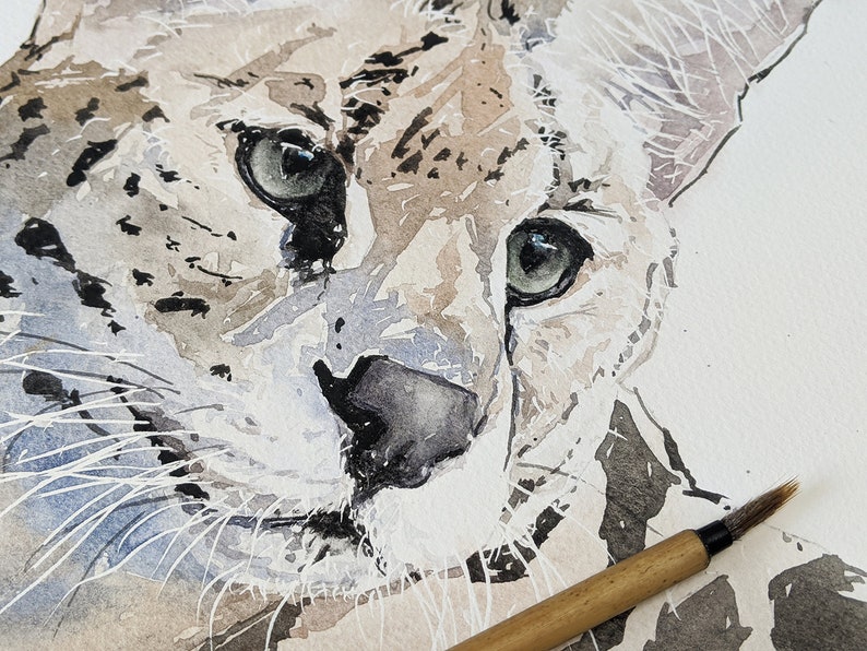Op de afbeelding: Close-up aquarel schilderij van het gezicht van een serval. De serval heeft grote, groene ogen en een zwarte neus. Het schilderij is gemaakt in tinten bruin, grijs en wit.
