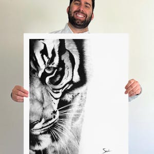 May include: A black and white art print featuring a detailed close-up of a tiger's face on the left side, with the right side left as a blank white space. The tiger has sharp, dark stripes and visible whiskers. A small signature is in the bottom right.