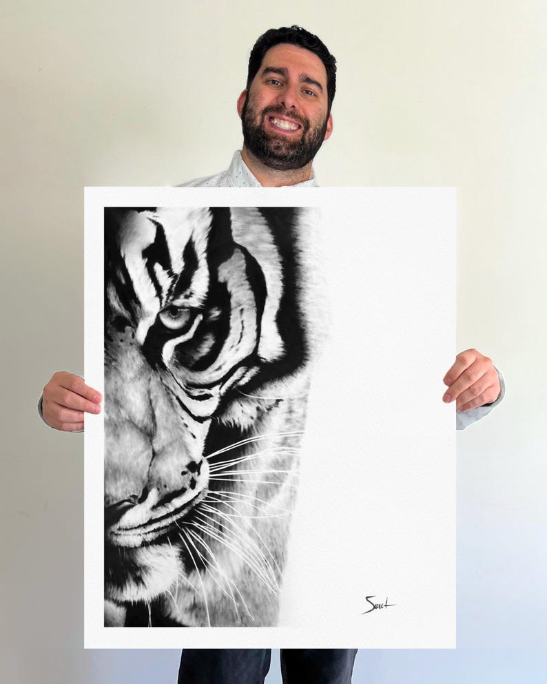 May include: A black and white art print featuring a detailed close-up of a tiger's face on the left side, with the right side left as a blank white space. The tiger has sharp, dark stripes and visible whiskers. A small signature is in the bottom right.
