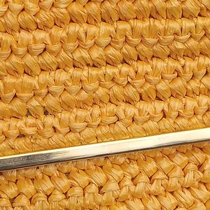 Pode incluir: Close-up de uma bolsa amarela tecida com um fecho de metal dourado. A bolsa &eacute; feita de um material tecido apertado, criando uma superf&iacute;cie texturizada.