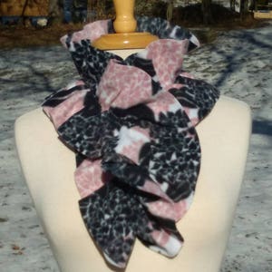 May include: A black and pink patterned fleece neck warmer with a ruffled design.