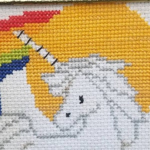 May include: A white unicorn cross-stitch with a rainbow background. The unicorn is facing left and has a black horn and eye. The rainbow is red, orange, yellow, green, blue, indigo, and violet.