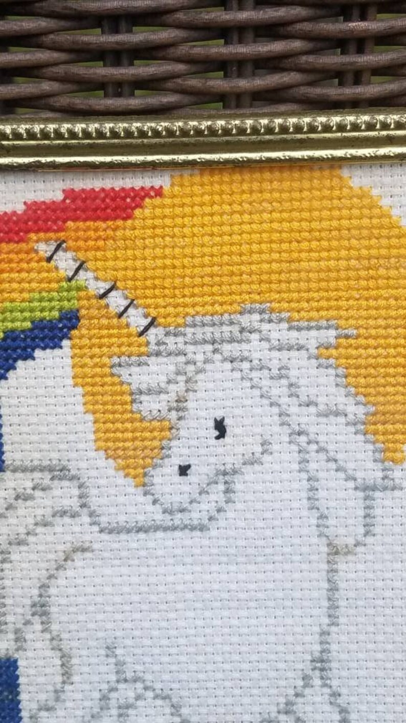 May include: A white unicorn cross-stitch with a rainbow background. The unicorn is facing left and has a black horn and eye. The rainbow is red, orange, yellow, green, blue, indigo, and violet.