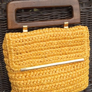 Pode incluir: Uma bolsa de m&atilde;o de croch&ecirc; amarela com uma al&ccedil;a de madeira e uma barra de metal dourado na frente.