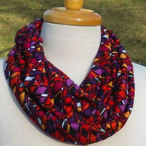 May include: A colorful infinity scarf with a geometric pattern in shades of red, orange, purple, and white on a black background.